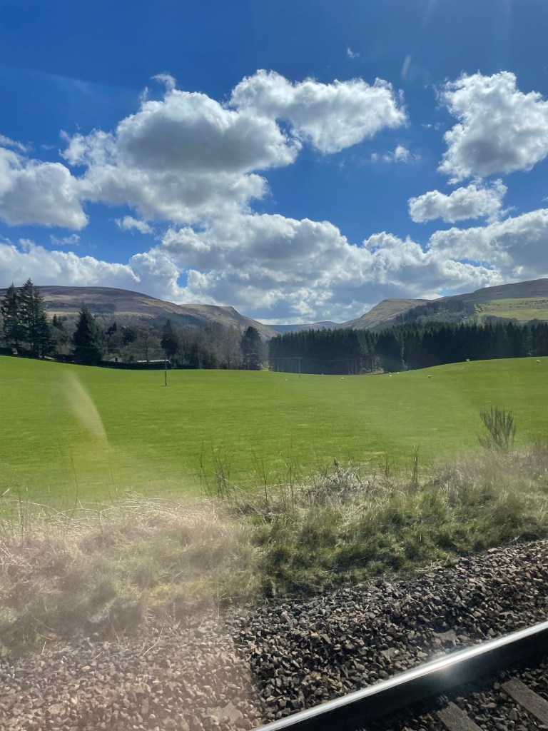 View from train window of some hills and fields