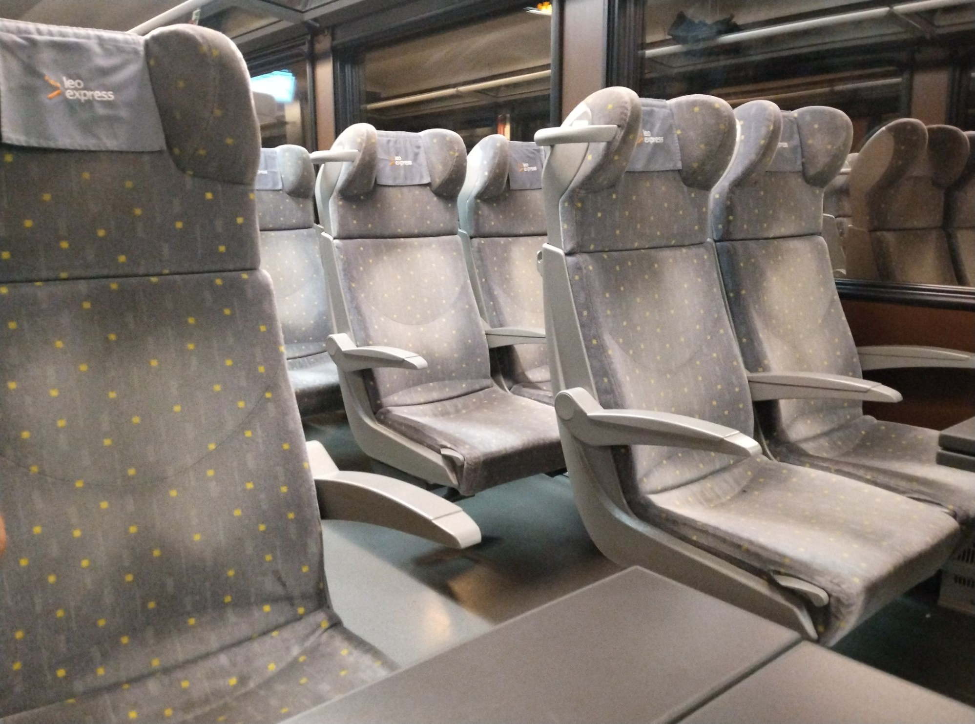 Grey seats onboard a train in both airline and table seat arrangements.