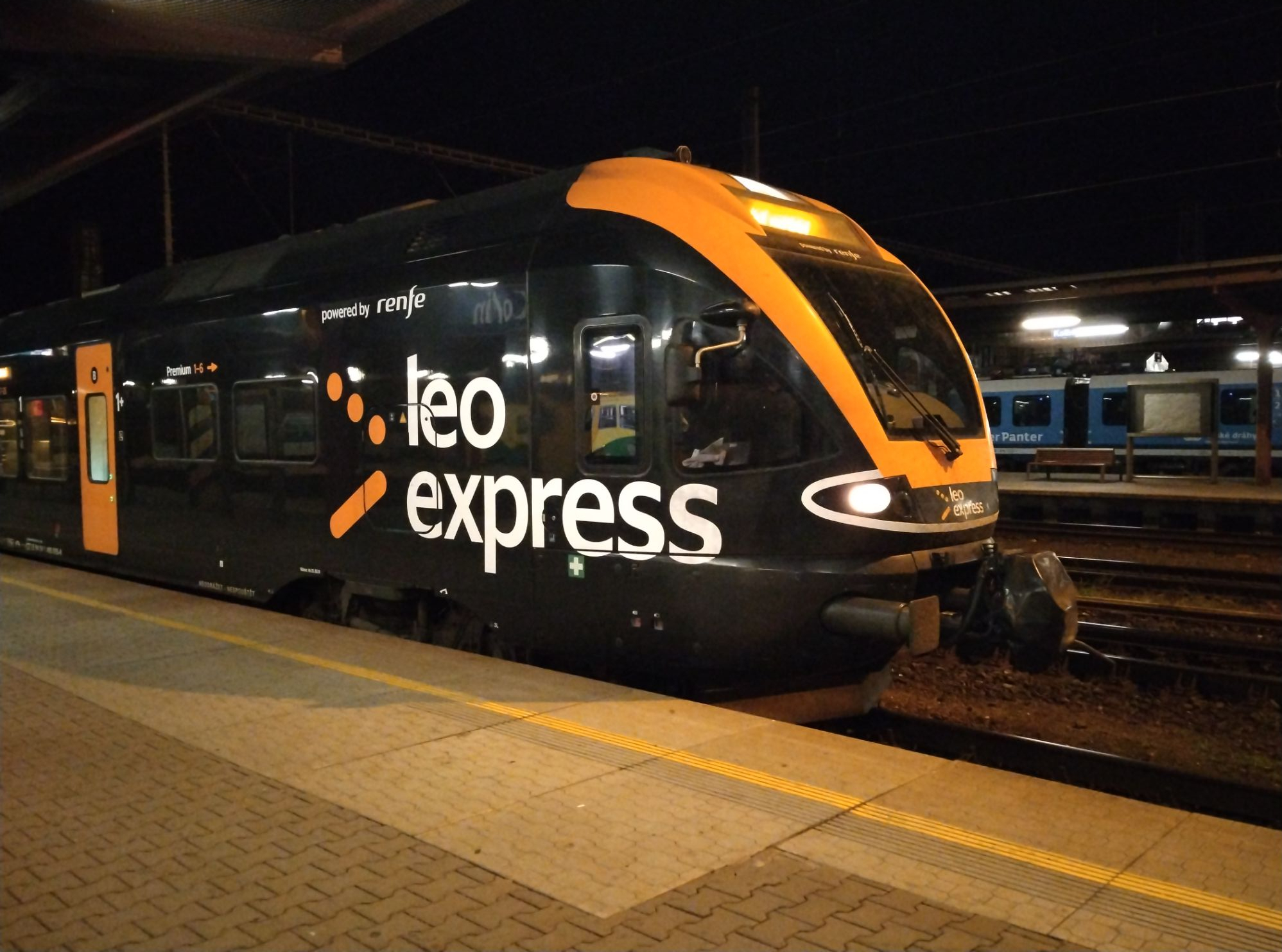 Black train with orange front sitting alongside the platform with Leo Express written on the side.