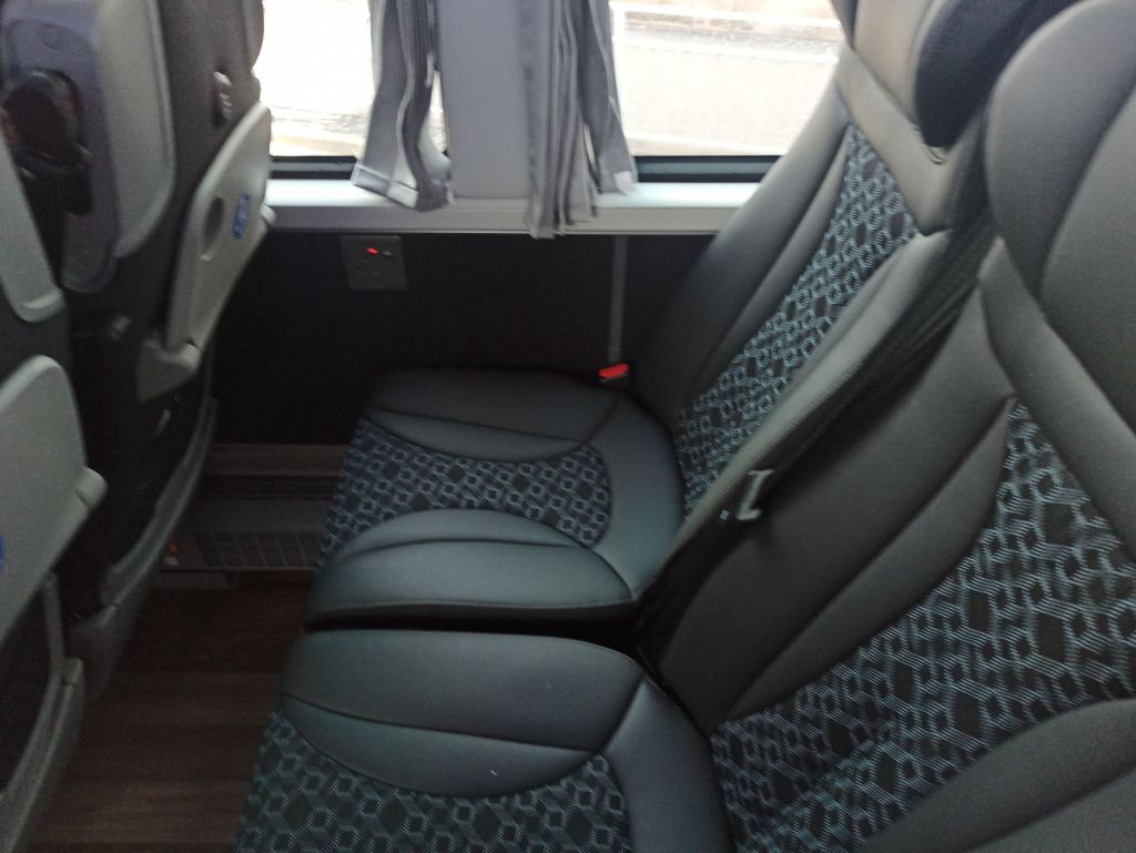 Picture of leather seats on Ember coach, seatbelt, grey tray table, USB charging port and socket all visible