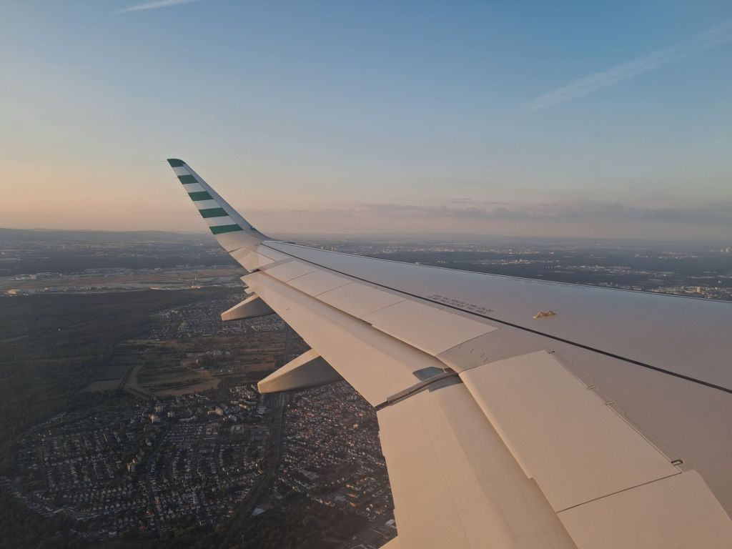 View of aircraft wing with airport in background and dusk sky.